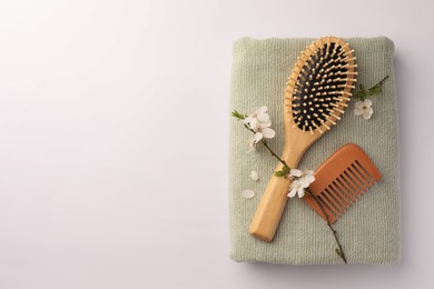 Photo of Wooden hairbrush, comb, towel and branch with flowers on white background, top view. Space for text