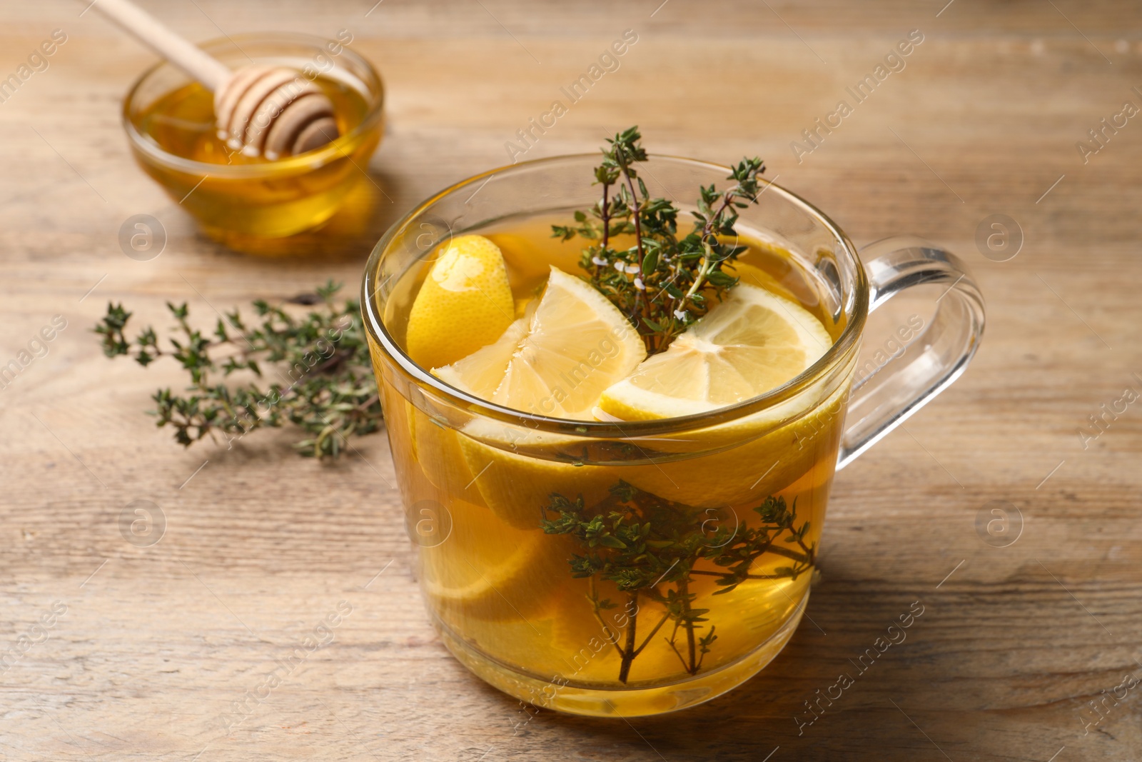 Photo of Fresh thyme tea with pieces of lemon on wooden table, closeup