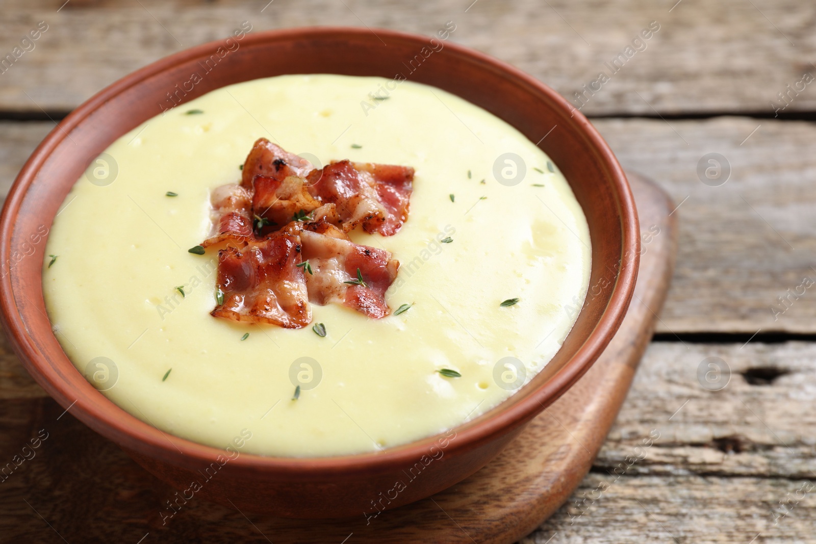 Photo of Tasty potato soup with bacon and rosemary in bowl on wooden table, closeup