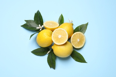Many fresh ripe lemons with green leaves on light blue background, flat lay