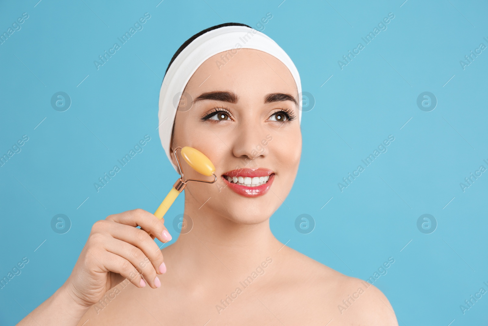 Photo of Woman using natural jade face roller on light blue background