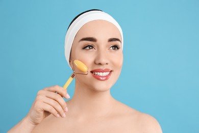 Woman using natural jade face roller on light blue background