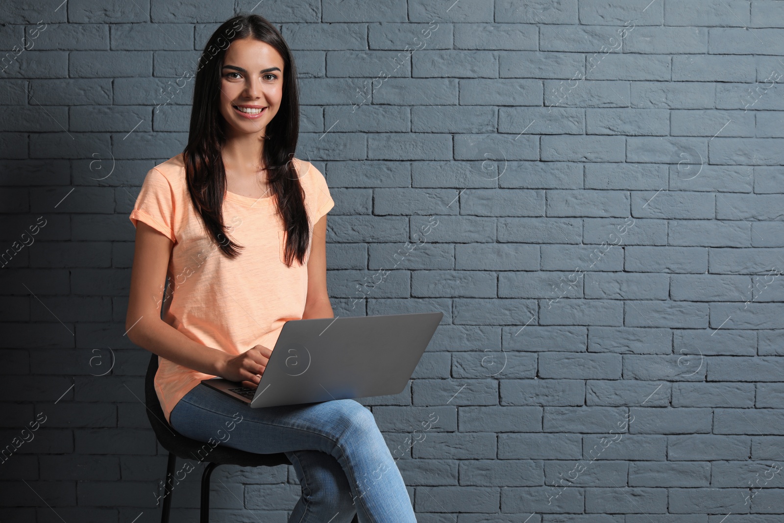 Photo of Young woman with modern laptop on brick wall background