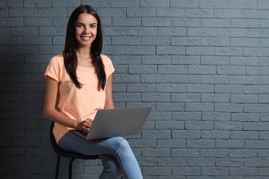 Young woman with modern laptop on brick wall background