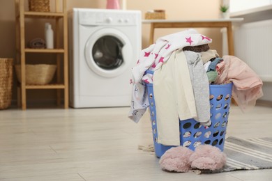 Photo of Laundry basket with baby clothes and fluffy slippers on wooden floor in bathroom, space for text