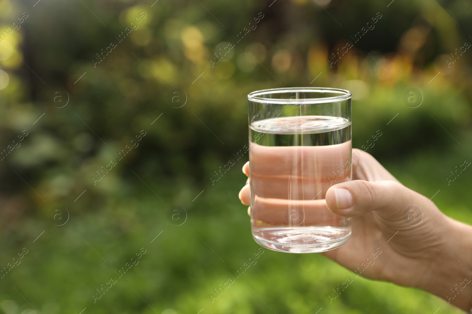 Photo of Woman holding glass of fresh water outdoors, closeup. Space for text