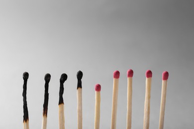 Photo of Burnt and whole matches on light grey background, closeup. Stop destruction by breaking chain reaction concept