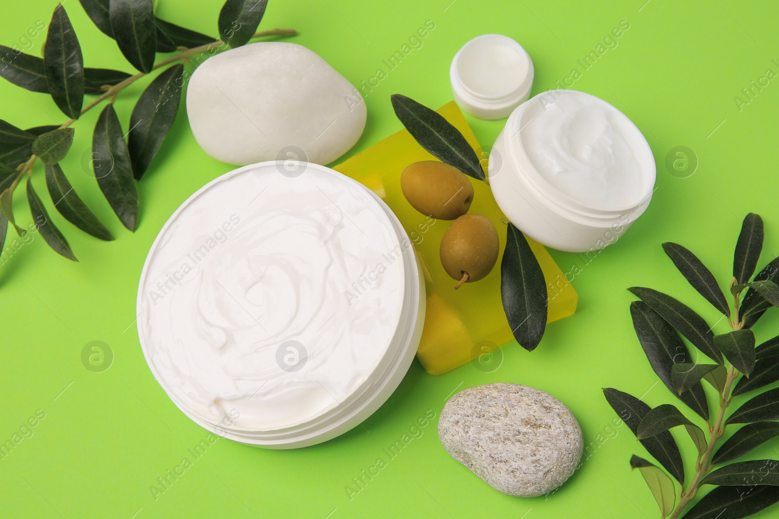Photo of Different cosmetic products with olives and stones on light green background, above view