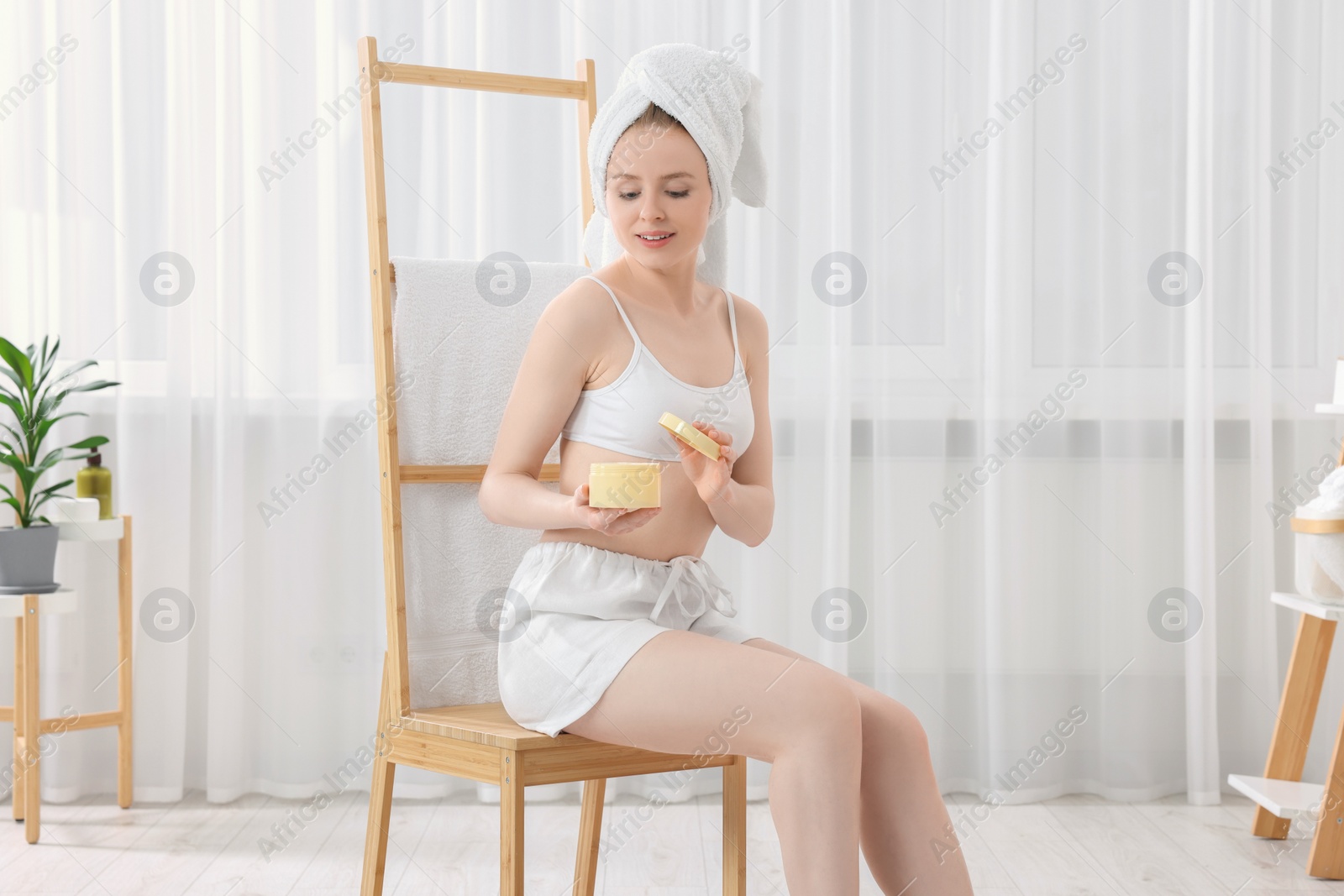 Photo of Beautiful young woman with jar of body cream indoors