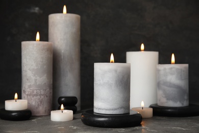 Photo of Burning candles and black spa stones on grey table