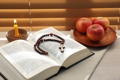 Photo of Bible with prayer beads, candle and apples near window indoors. Great Lent season
