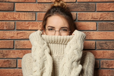 Photo of Beautiful young woman in warm sweater near brick wall