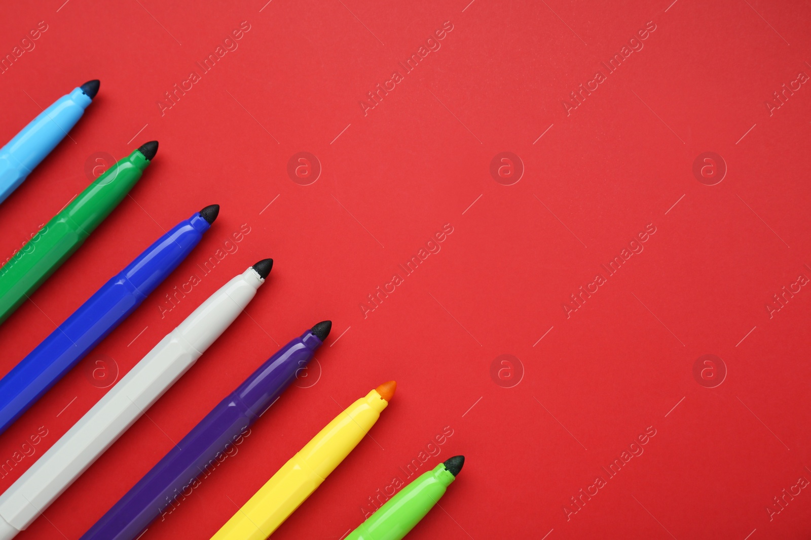 Photo of Different colorful markers on red background, flat lay. Space for text