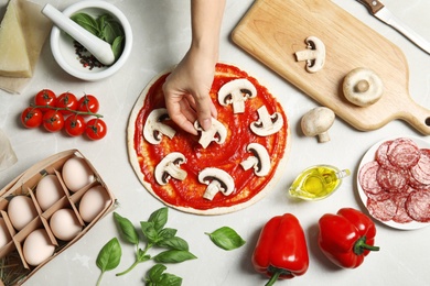 Photo of Woman putting mushrooms onto pizza crust with sauce on light table, top view