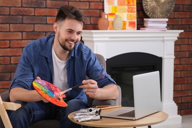 Photo of Happy man learning to draw with online course on laptop at home. Time for hobby