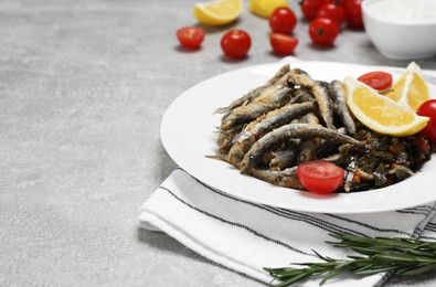 Photo of Delicious fried anchovies with cherry tomatoes and slices of lemon served on light grey table, closeup. Space for text