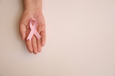 Senior woman holding pink ribbon on light background, top view with space for text. Breast cancer awareness