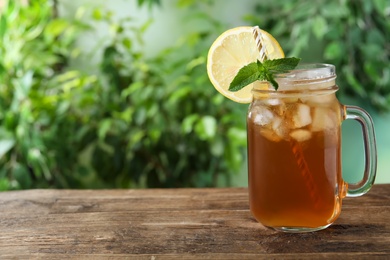 Photo of Delicious iced tea in mason jar on wooden table outdoors, space for text