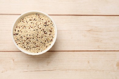 Photo of Raw quinoa seeds in bowl on wooden table, top view. Space for text