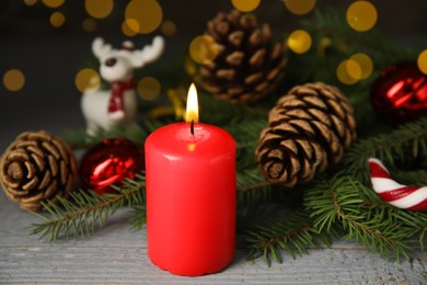 Photo of Burning candle and Christmas decor on wooden table against blurred festive lights