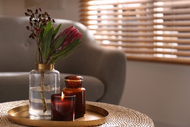 Vase with beautiful protea flower and candles on wicker stand indoors, space for text. Interior elements