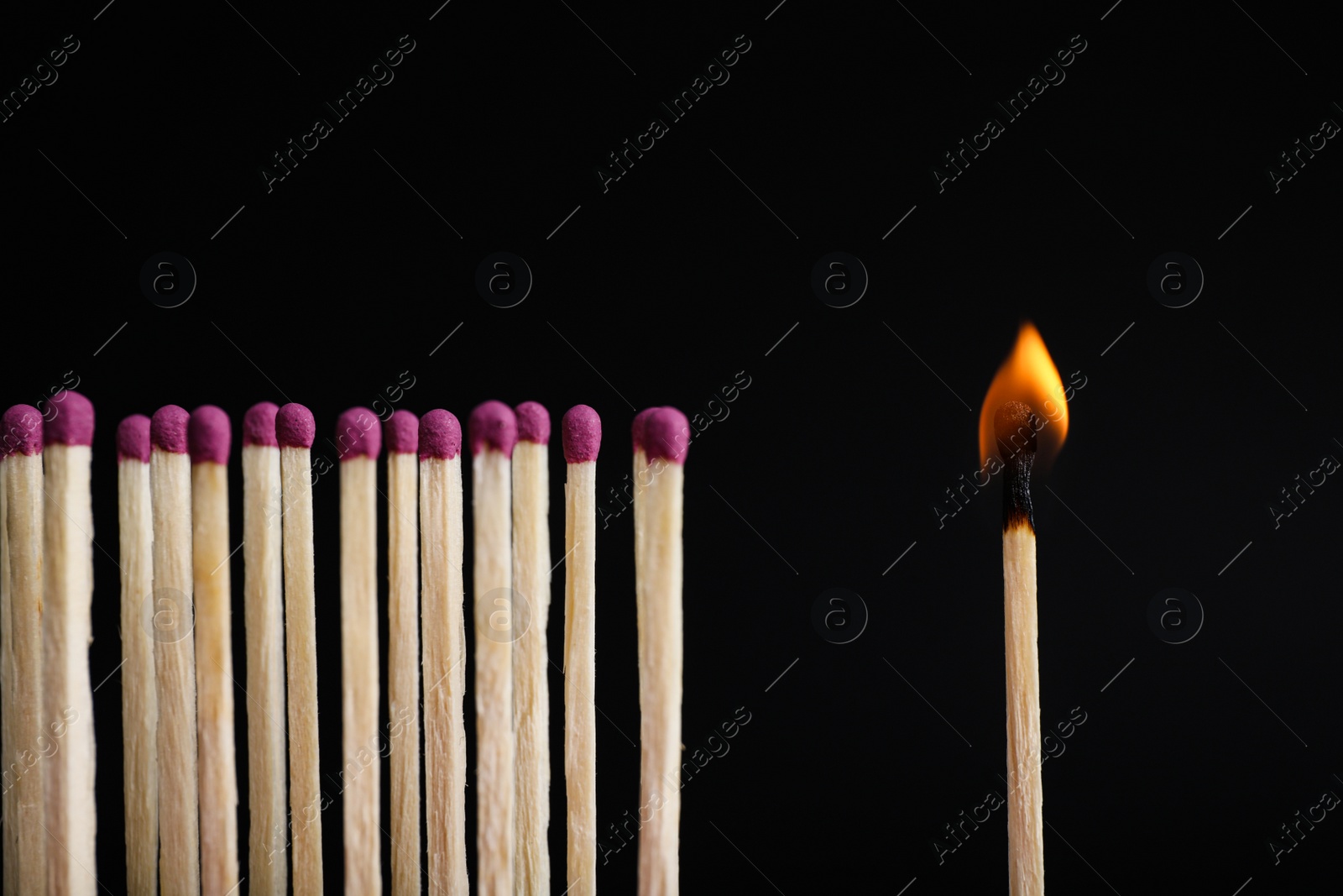 Photo of Burning match among others on black background