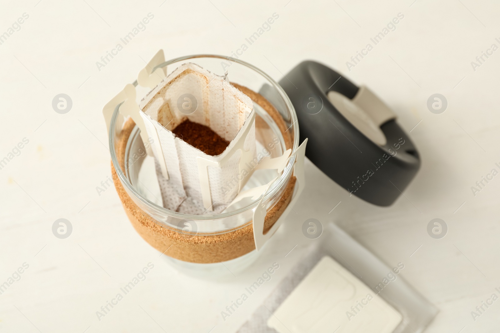 Photo of Drip coffee bag in glass cup on white table, closeup