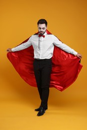 Man in scary vampire costume with fangs posing on orange background. Halloween celebration