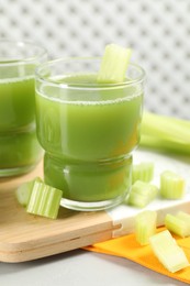 Celery juice and fresh vegetables on light gray table, closeup