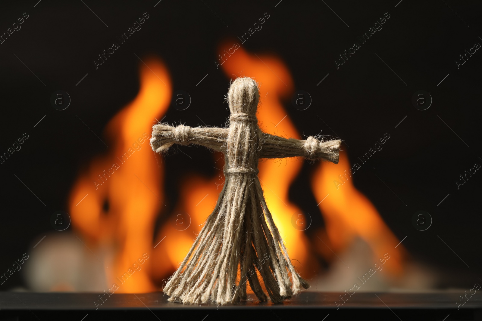 Photo of Voodoo doll on black table against blurred flame. Curse ceremony