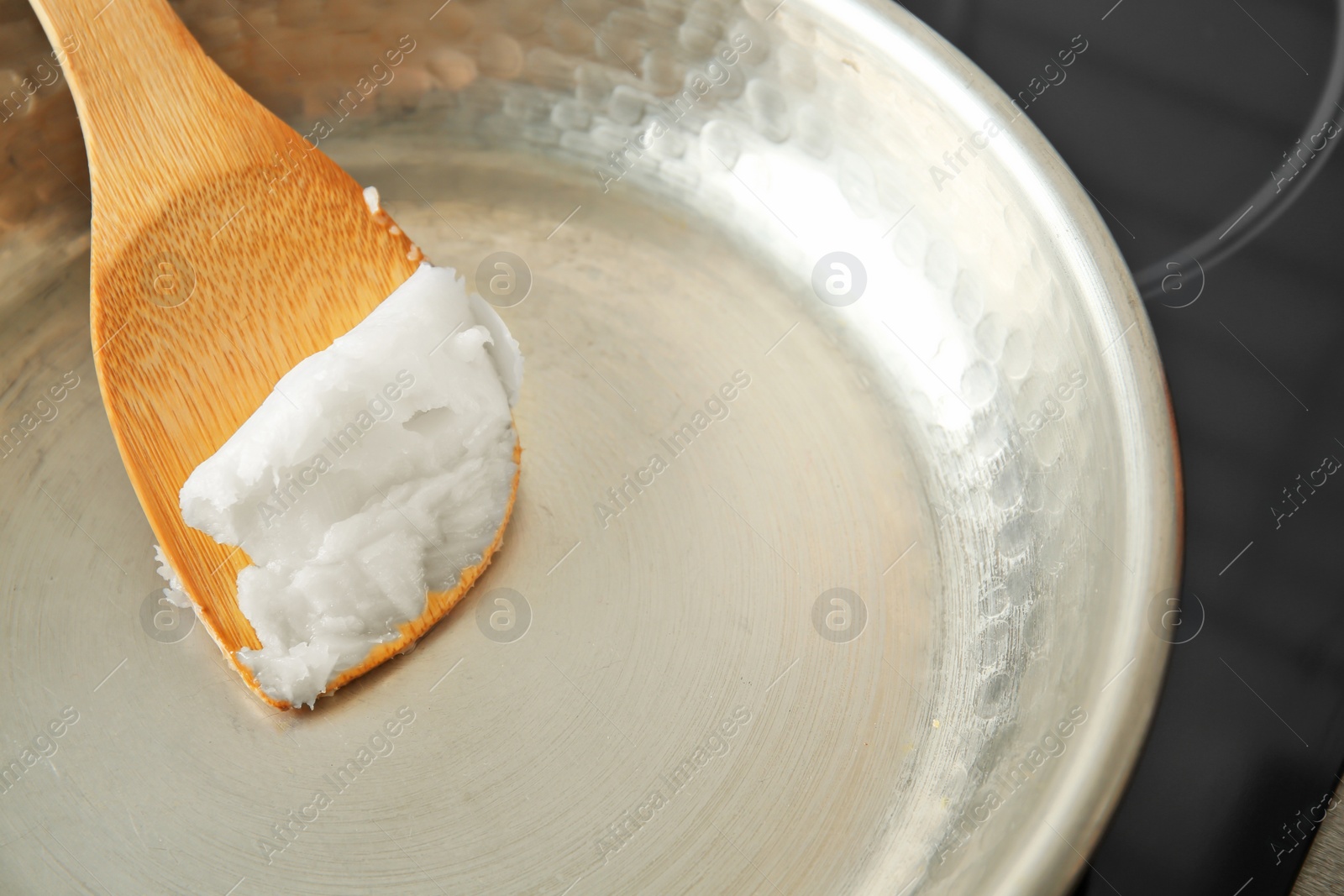 Photo of Wooden spatula with coconut oil in frying pan, closeup. Healthy cooking