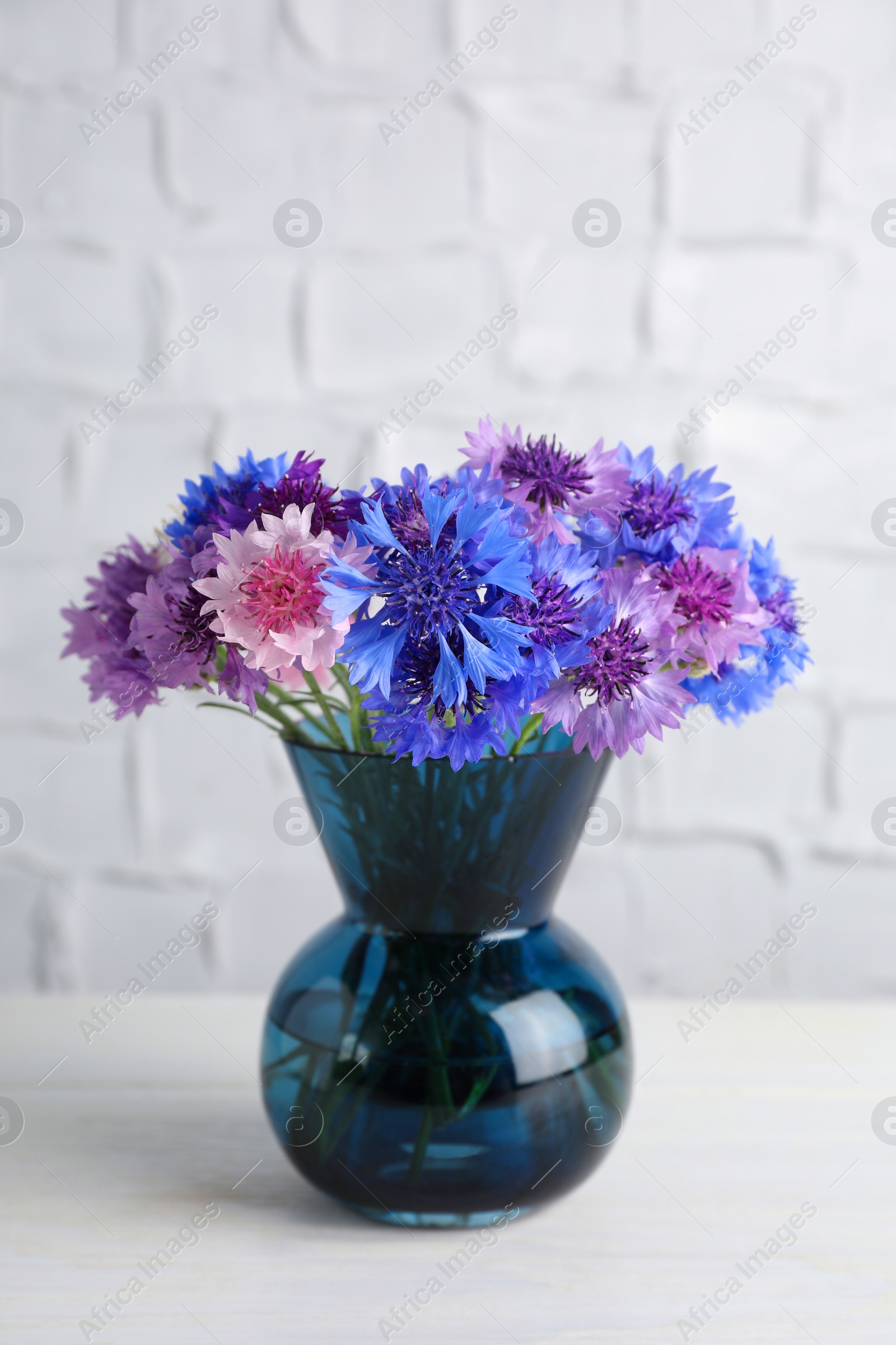 Photo of Bouquet of beautiful cornflowers in glass vase on white wooden table