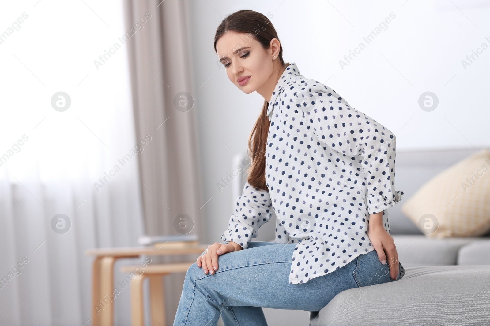 Photo of Young woman suffering from hemorrhoid at home. Space for text