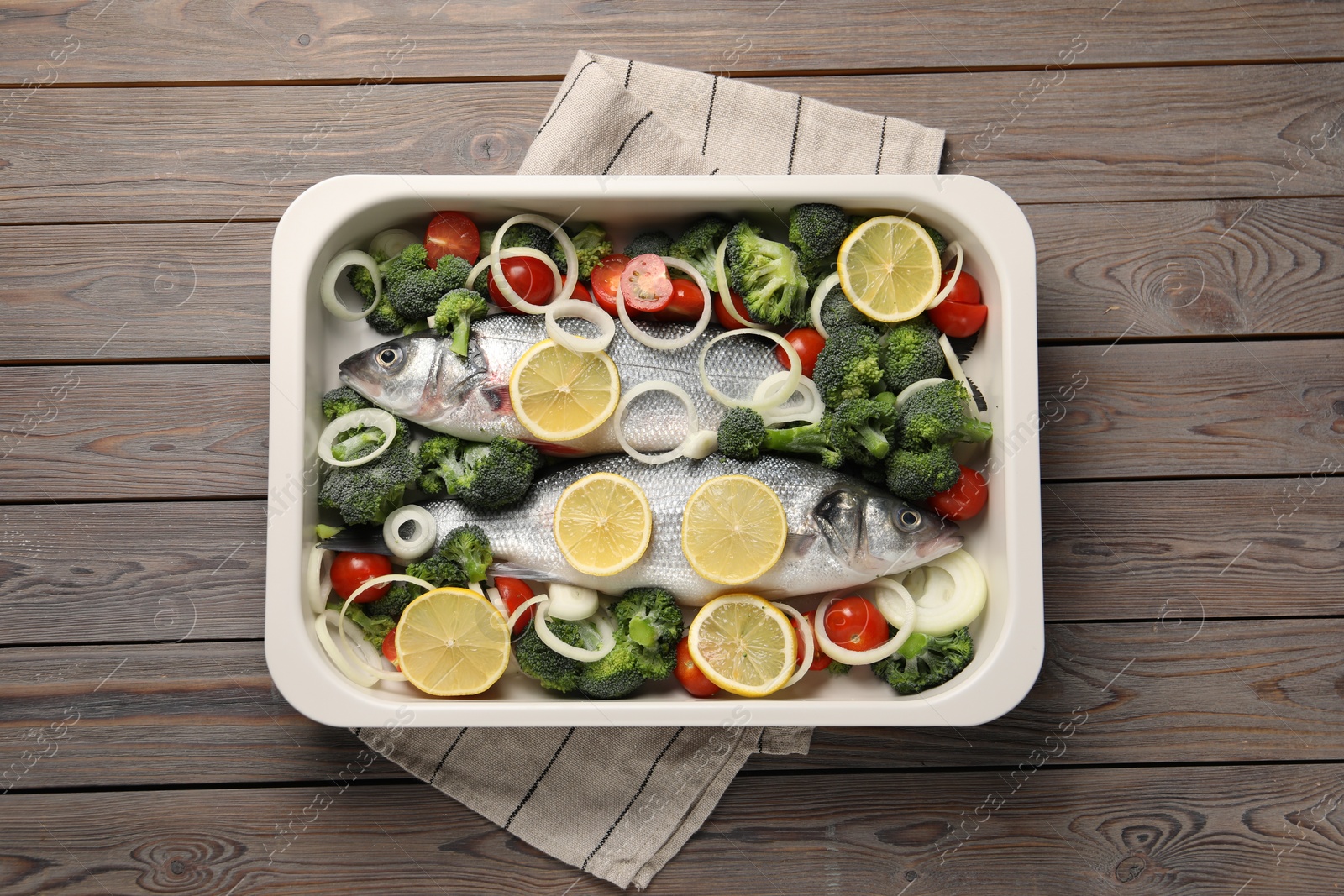 Photo of Raw fish with vegetables and lemon in baking dish on wooden table, top view