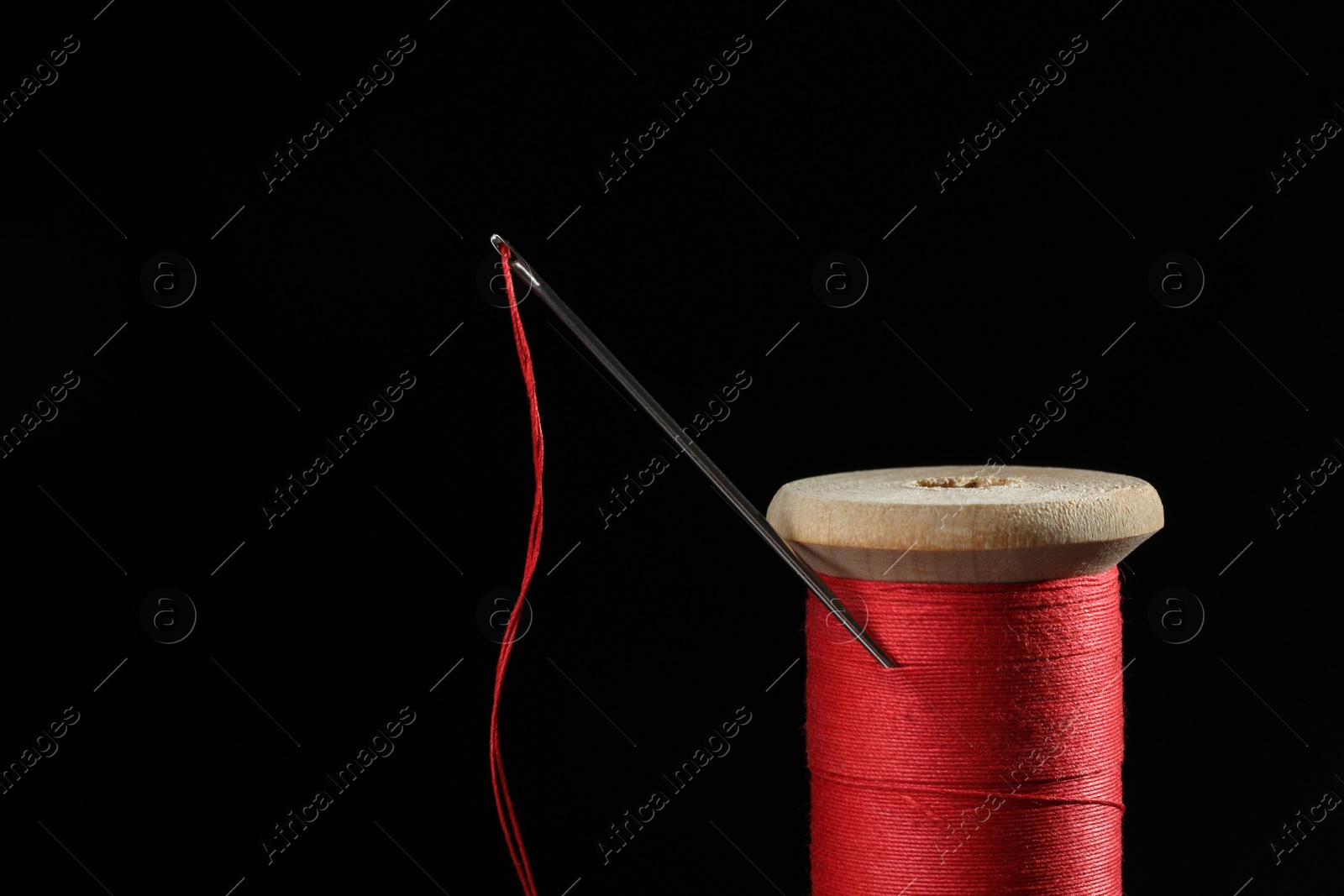 Photo of Red sewing thread with needle on black background, closeup