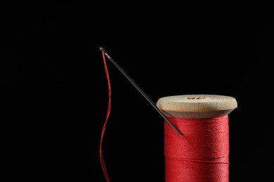 Red sewing thread with needle on black background, closeup