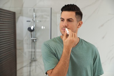 Photo of Man applying hygienic lip balm in bathroom
