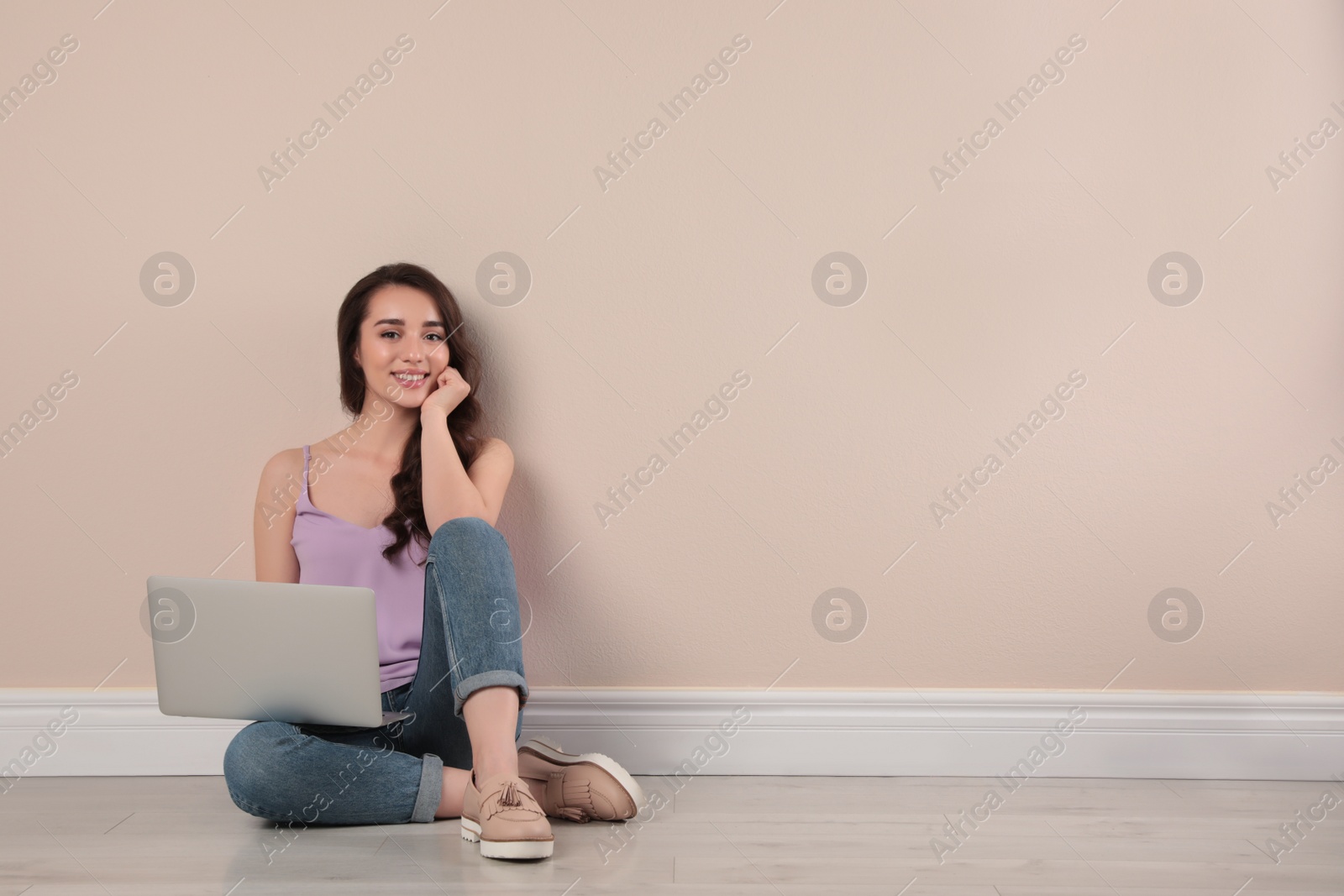 Photo of Young woman sitting with laptop near beige wall. Space for text