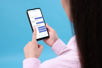 Woman texting with friend using messaging application on smartphone against light blue background, closeup