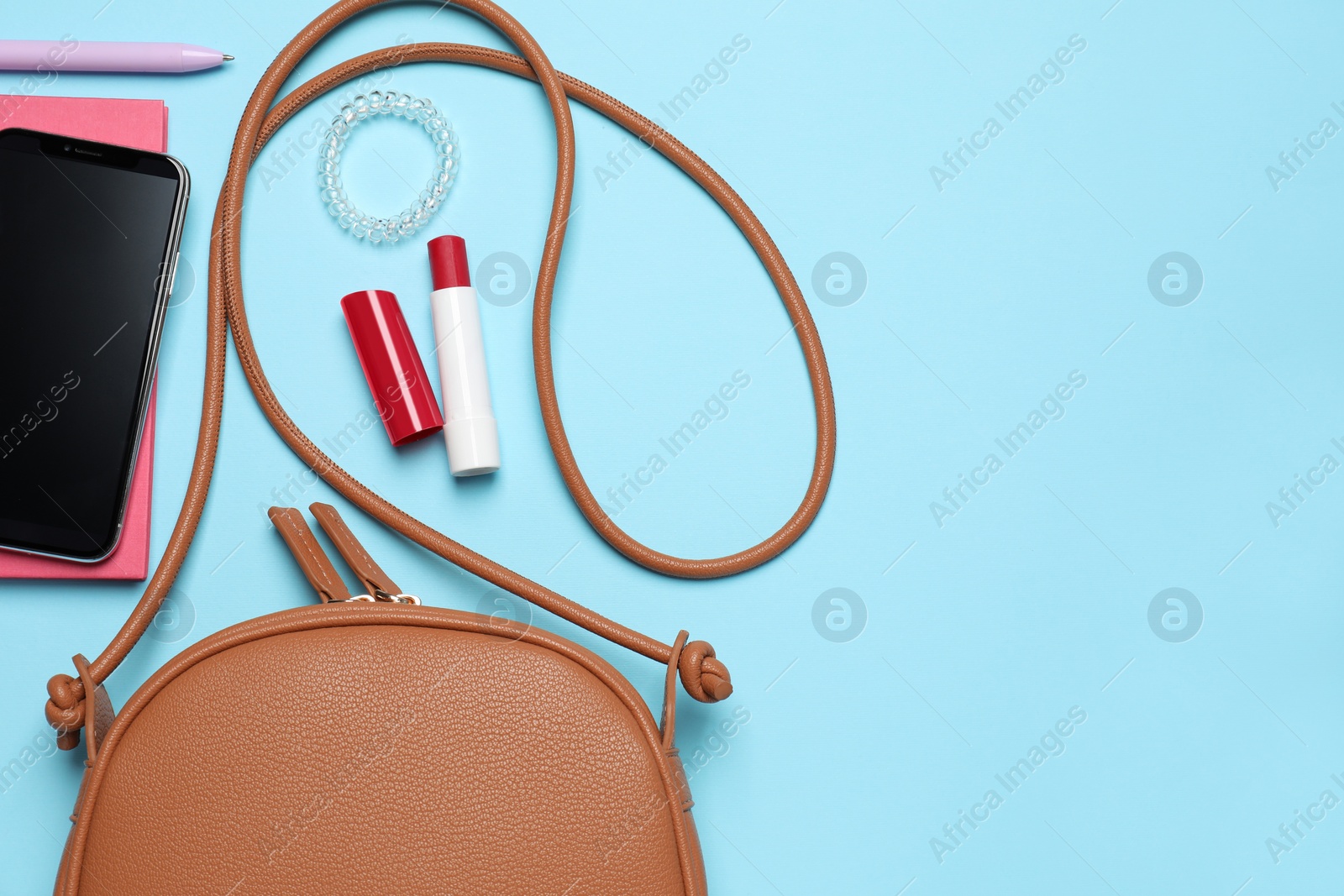 Photo of Stylish woman's bag with smartphone and accessories on light blue background, flat lay. Space for text