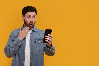 Photo of Surprised man with smartphone on orange background. Space for text