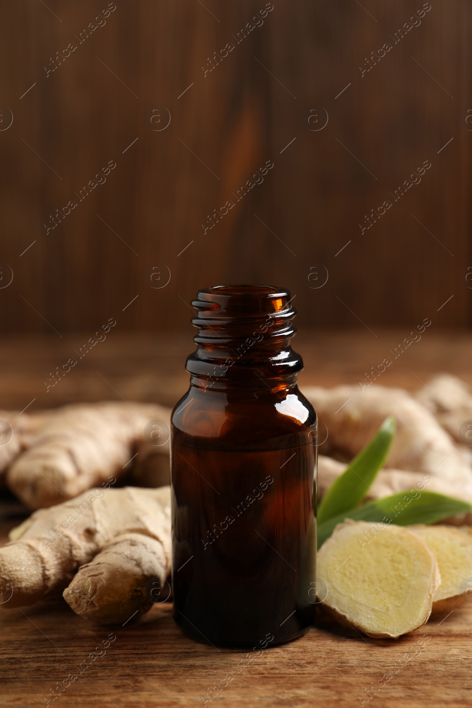 Photo of Glass bottle of essential oil and ginger root on wooden table