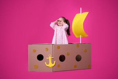 Photo of Little child playing with ship made of cardboard box on pink background