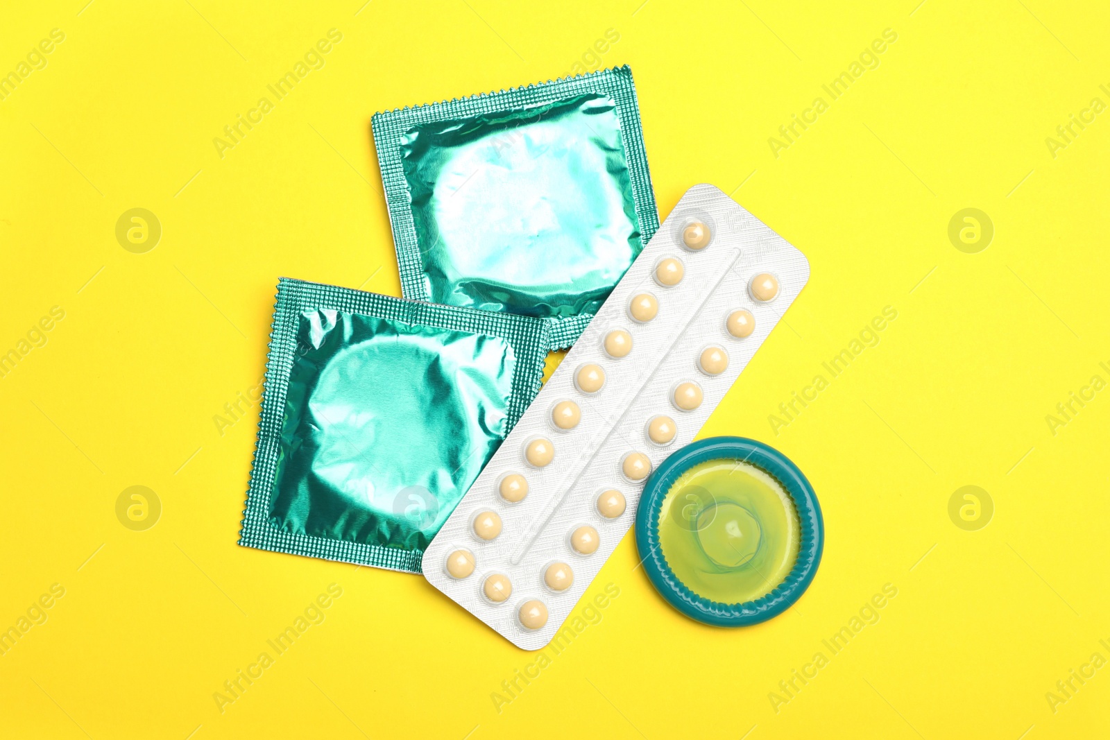 Photo of Condoms and birth control pills on yellow background, flat lay. Safe sex concept