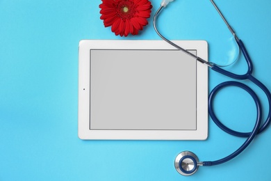 Photo of Tablet, flower and stethoscope on light blue background, flat lay. Gynecological care