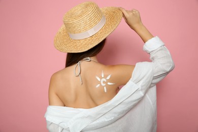 Photo of Teenage girl with sun protection cream on her back against pink background