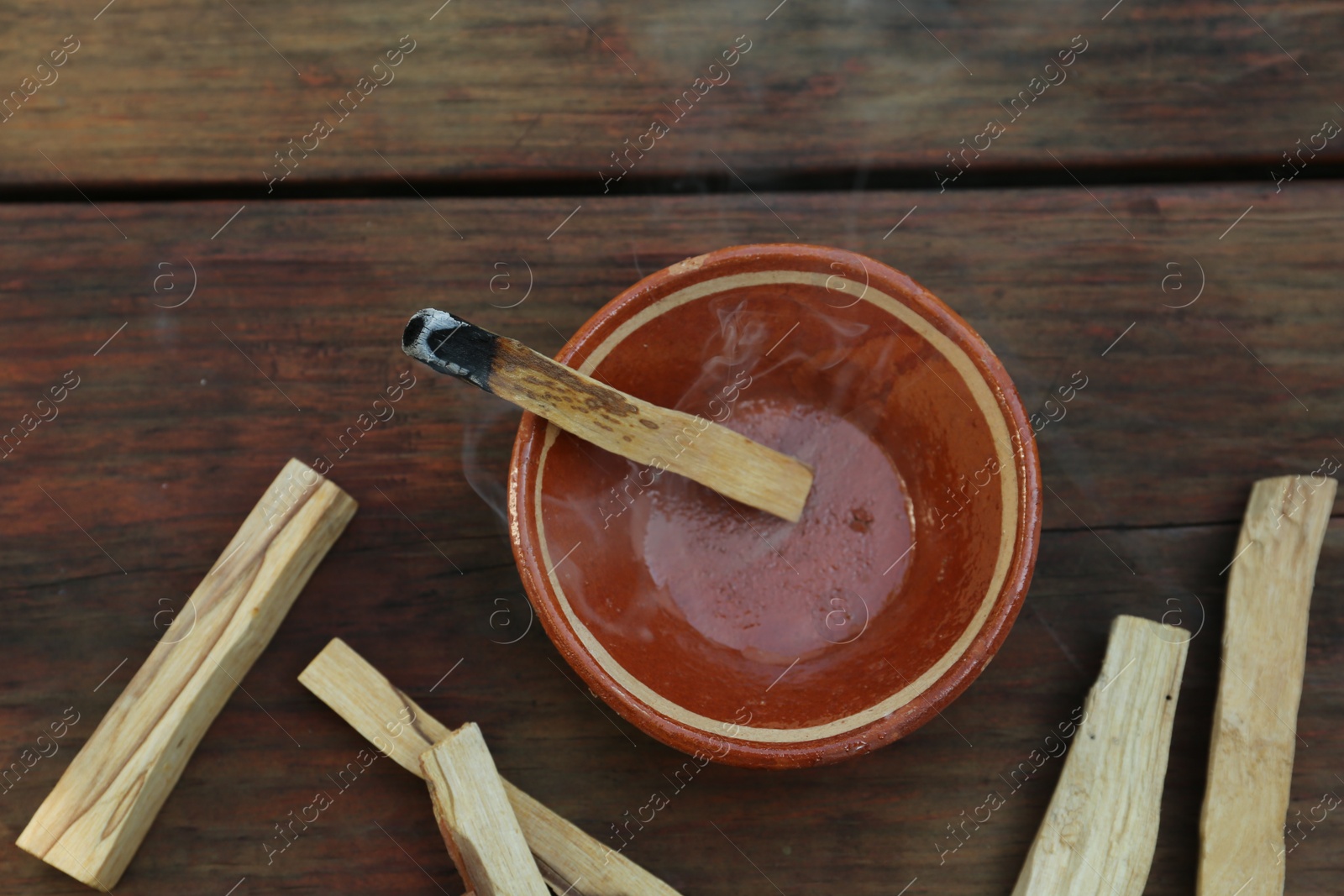 Photo of Palo santo stick smoldering in bowl on wooden table, flat lay