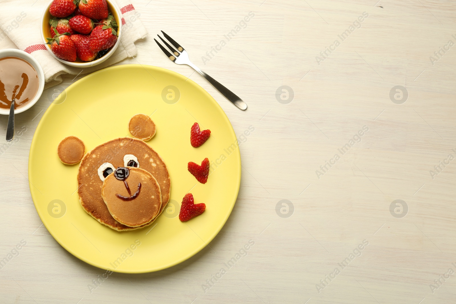 Photo of Creative serving for kids. Plate with strawberries, cute bear made of pancakes on light wooden table, flat lay. Space for text