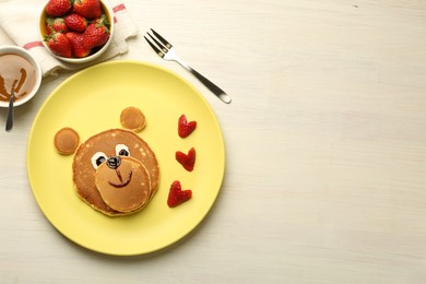 Creative serving for kids. Plate with strawberries, cute bear made of pancakes on light wooden table, flat lay. Space for text