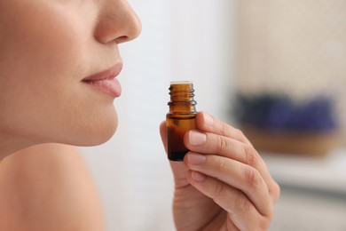 Woman with bottle of essential oil on blurred background, closeup